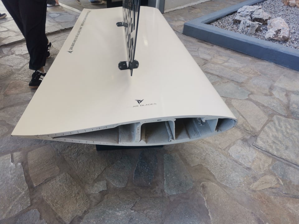 A wind turbine blade upcycled into a bench, showcased outside a corporate training centre in Athens. This is fine, but we would need hundreds of thousands of benches to find a use for all these blades that have already stopped moving, not to mention to close and rewild all the roads - hundreds of thousands of kilometres - that were opened to install them on mountain tops throughout Greece.